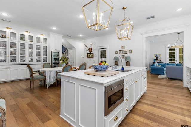 kitchen with light hardwood / wood-style floors, a center island with sink, sink, stainless steel microwave, and white cabinets