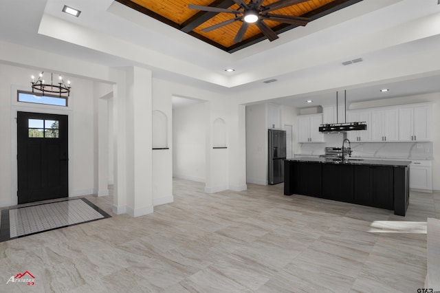 kitchen featuring extractor fan, white cabinets, a center island with sink, decorative backsplash, and wooden ceiling