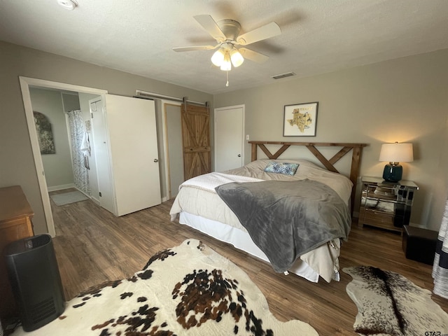 bedroom with a barn door, dark wood-type flooring, a textured ceiling, and ceiling fan