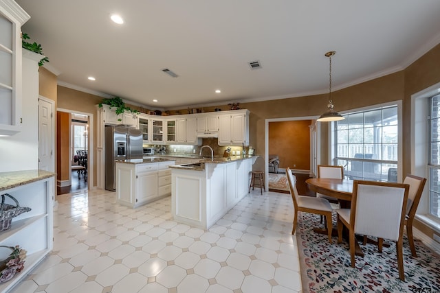 kitchen with stainless steel fridge, a healthy amount of sunlight, a center island with sink, decorative light fixtures, and white cabinetry