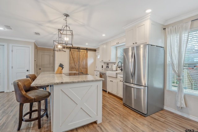 kitchen featuring stainless steel appliances, a kitchen island, a barn door, light hardwood / wood-style flooring, and white cabinets