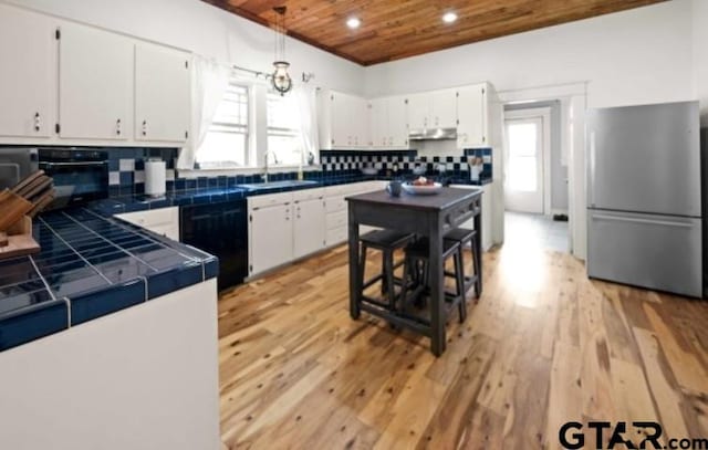 kitchen with stainless steel fridge, tile countertops, white cabinetry, and wooden ceiling