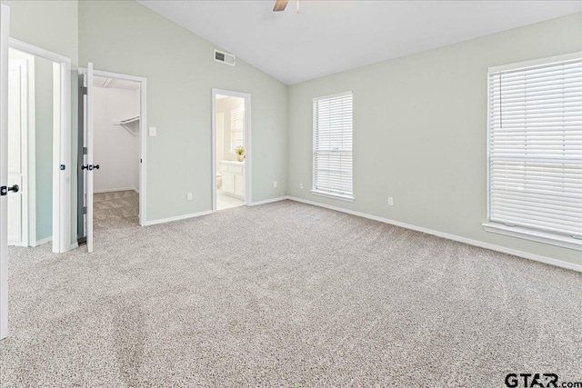 unfurnished bedroom with vaulted ceiling, a spacious closet, ceiling fan, light carpet, and ensuite bath