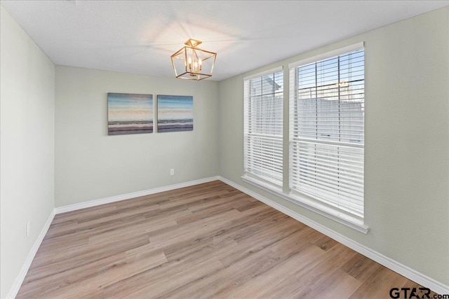 spare room with an inviting chandelier and light hardwood / wood-style floors