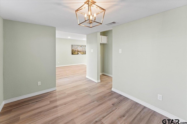 empty room featuring an inviting chandelier and light wood-type flooring