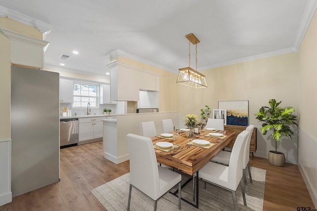 dining space with sink, light hardwood / wood-style floors, and ornamental molding