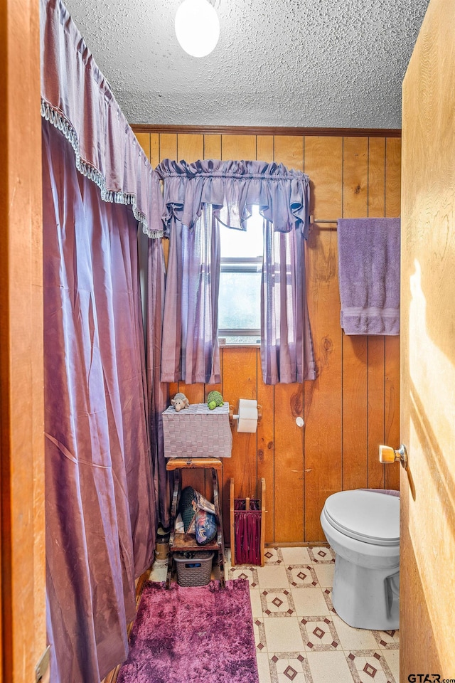 bathroom featuring toilet, a textured ceiling, and wooden walls