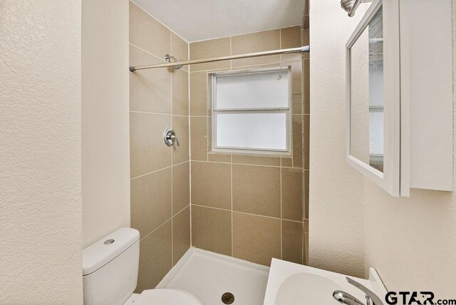 bathroom featuring toilet, sink, and a tile shower