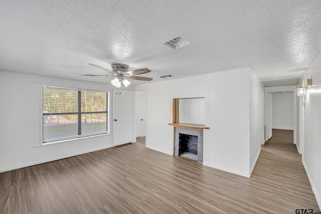 1005 N Rodeo St, Gladewater, TX 75647 - unfurnished living room featuring a textured ceiling, wood finished floors, ceiling fan, baseboards, and a fireplace