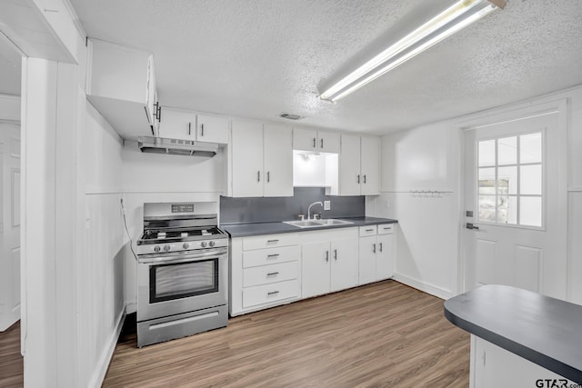 1005 N Rodeo St, Gladewater, TX 75647 - kitchen with stainless steel gas range, a sink, under cabinet range hood, dark countertops, and light wood-style flooring
