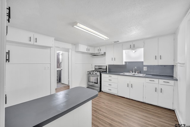 1005 N Rodeo St, Gladewater, TX 75647 - kitchen featuring stainless steel gas range oven, a sink, dark countertops, under cabinet range hood, and light wood-style flooring