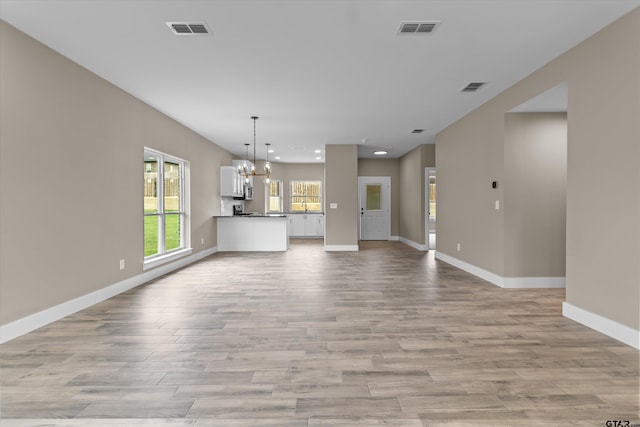 unfurnished living room featuring light wood-type flooring and a chandelier