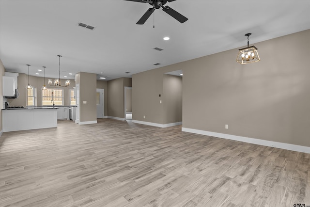 unfurnished living room with light wood-type flooring and ceiling fan with notable chandelier