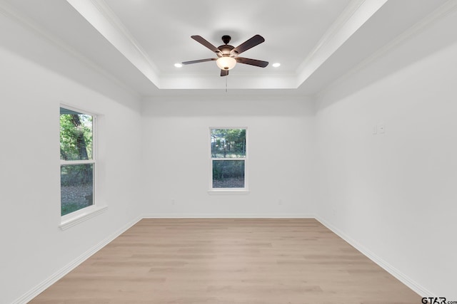 spare room featuring a tray ceiling, ceiling fan, crown molding, and light wood-type flooring