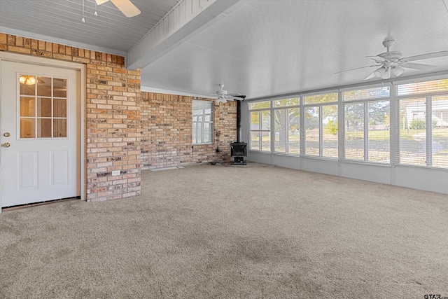 unfurnished living room featuring beam ceiling, a wood stove, carpet floors, and brick wall