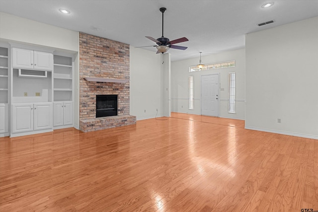 unfurnished living room featuring built in features, a brick fireplace, light hardwood / wood-style flooring, and ceiling fan