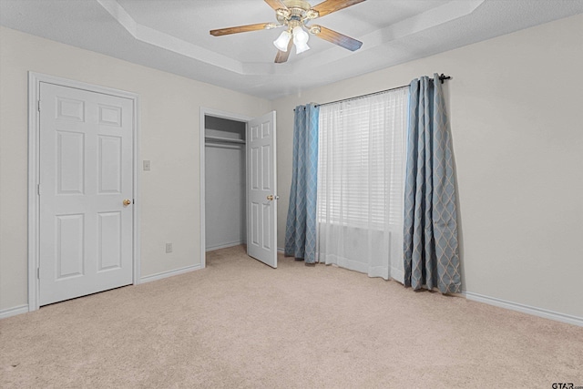 unfurnished bedroom with light colored carpet, a raised ceiling, and ceiling fan