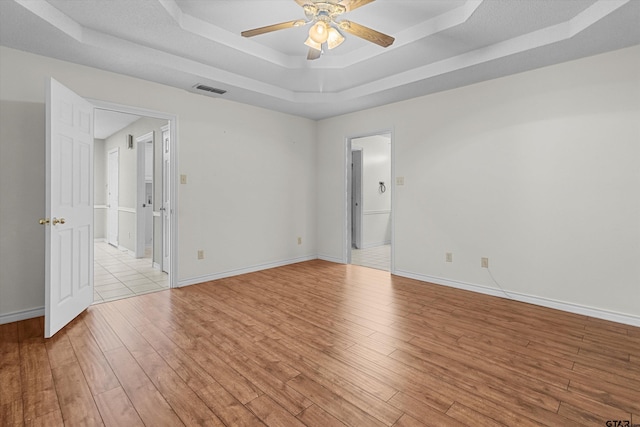 spare room with a tray ceiling, ceiling fan, and light hardwood / wood-style flooring