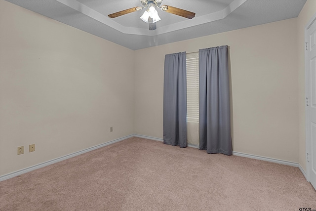 spare room featuring ceiling fan, light colored carpet, and a tray ceiling