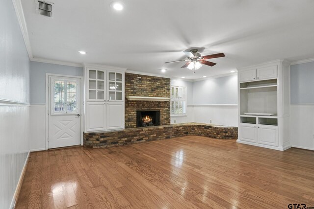 909 Elizabeth St, Gilmer, TX 75644 - unfurnished living room with a ceiling fan, a wainscoted wall, wood finished floors, crown molding, and a brick fireplace