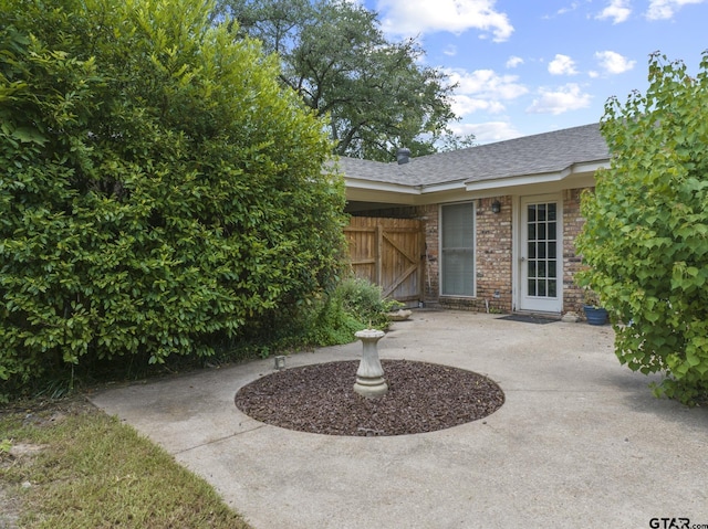 909 Elizabeth St, Gilmer, TX 75644 - view of exterior entry with a shingled roof, brick siding, a patio area, and fence