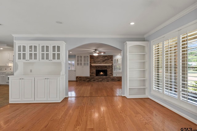 unfurnished living room with light hardwood / wood-style floors, built in shelves, ornamental molding, ceiling fan, and a fireplace