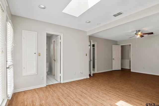 empty room with a wealth of natural light, light hardwood / wood-style floors, ceiling fan, and a skylight