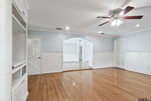 909 Elizabeth St, Gilmer, TX 75644 - empty room with arched walkways, a ceiling fan, light wood-style floors, wainscoting, and ornamental molding