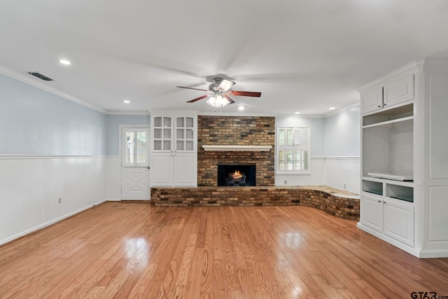 unfurnished living room featuring ornamental molding, a fireplace, light hardwood / wood-style floors, and ceiling fan