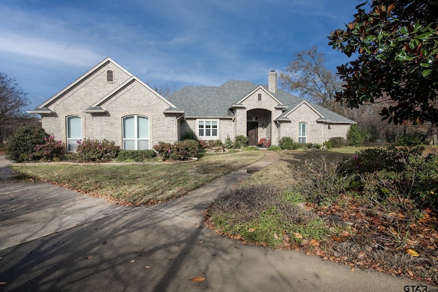 french country style house featuring a front yard, a chimney, and brick siding