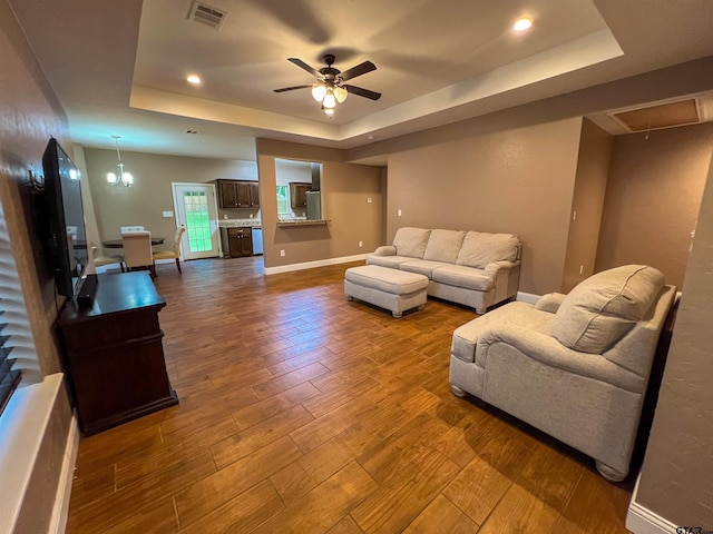 living room with ceiling fan with notable chandelier, hardwood / wood-style floors, and a tray ceiling