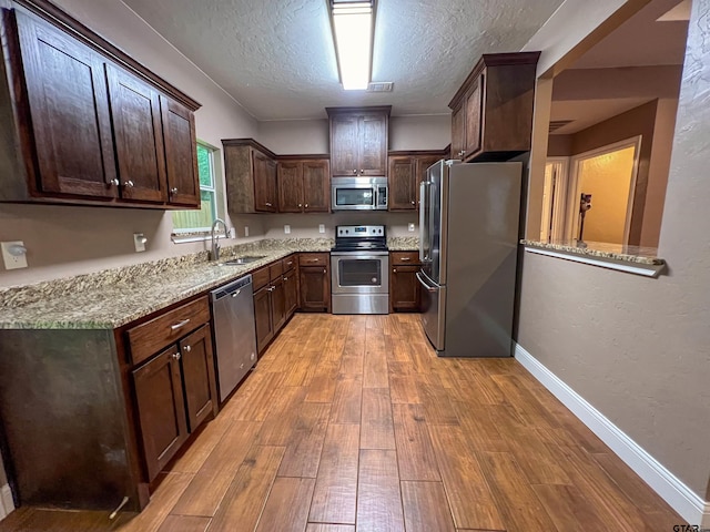 kitchen with light hardwood / wood-style floors, sink, light stone counters, and appliances with stainless steel finishes