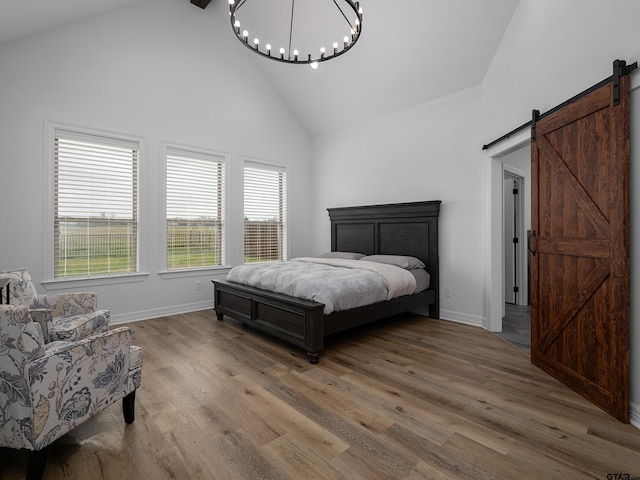 bedroom with light wood finished floors, baseboards, a barn door, an inviting chandelier, and high vaulted ceiling