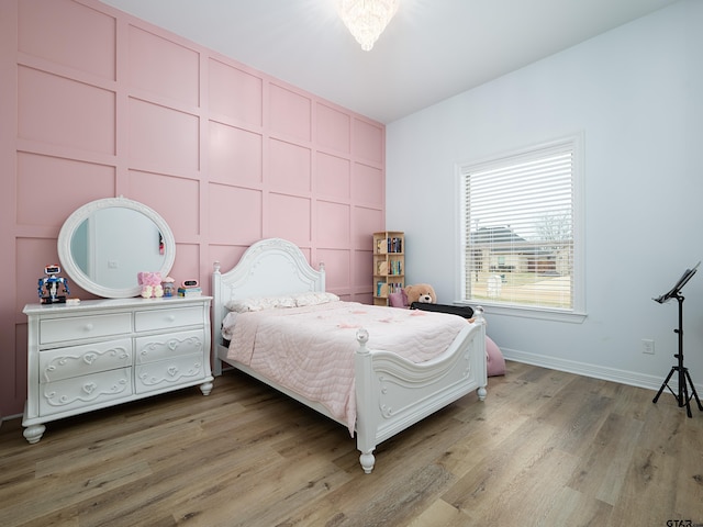 bedroom featuring a decorative wall, baseboards, and wood finished floors