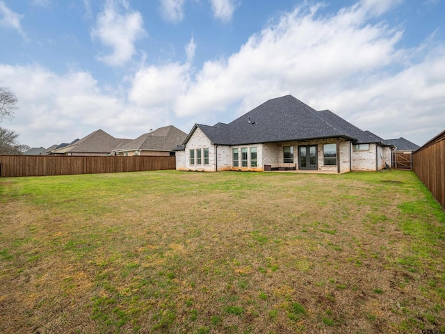 rear view of property with french doors, a lawn, a fenced backyard, and brick siding