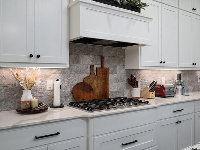 kitchen with light stone countertops, premium range hood, decorative backsplash, stainless steel gas stovetop, and white cabinetry