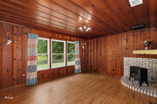 unfurnished living room featuring wood-type flooring, wooden ceiling, wooden walls, and a wood stove