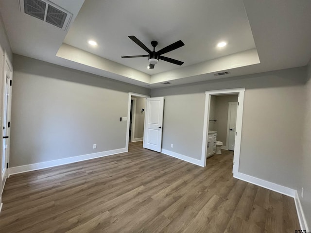 unfurnished bedroom featuring hardwood / wood-style floors, a tray ceiling, ceiling fan, and ensuite bathroom