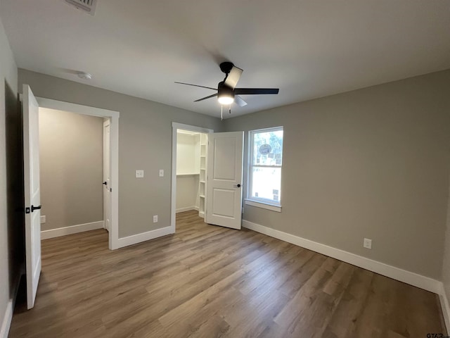 unfurnished bedroom with ceiling fan, light hardwood / wood-style floors, a walk in closet, and a closet