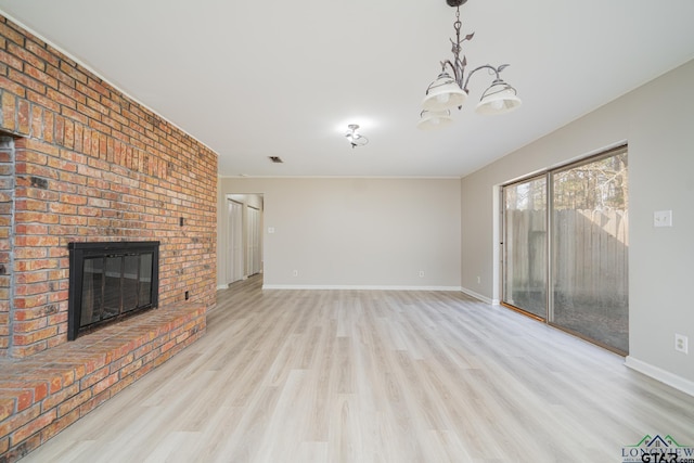 unfurnished living room featuring a brick fireplace, a notable chandelier, and light hardwood / wood-style flooring