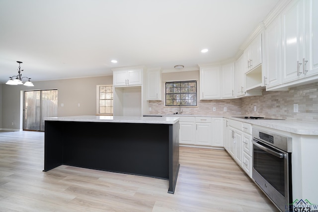 kitchen featuring a kitchen island, white cabinetry, sink, hanging light fixtures, and stainless steel oven