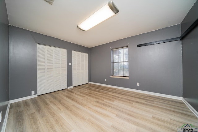 unfurnished bedroom featuring multiple closets and light hardwood / wood-style flooring