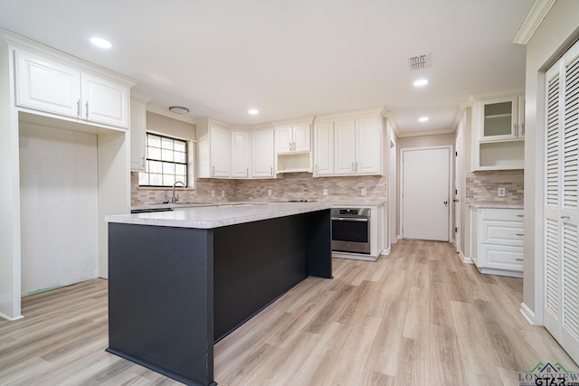 kitchen with stainless steel oven, light wood-type flooring, a kitchen island, decorative backsplash, and white cabinets