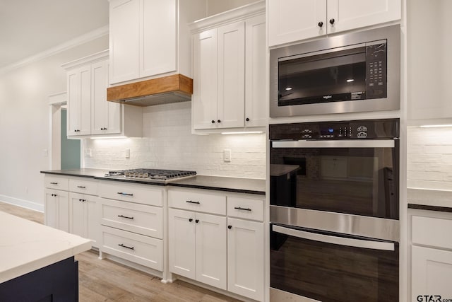 14738 Woodland Creek Dr, Tyler, TX 75706 - kitchen featuring stainless steel appliances, crown molding, white cabinetry, decorative backsplash, and light wood-style floors