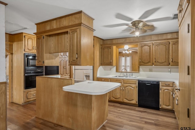 kitchen with wood finished floors, a sink, black appliances, light countertops, and a center island