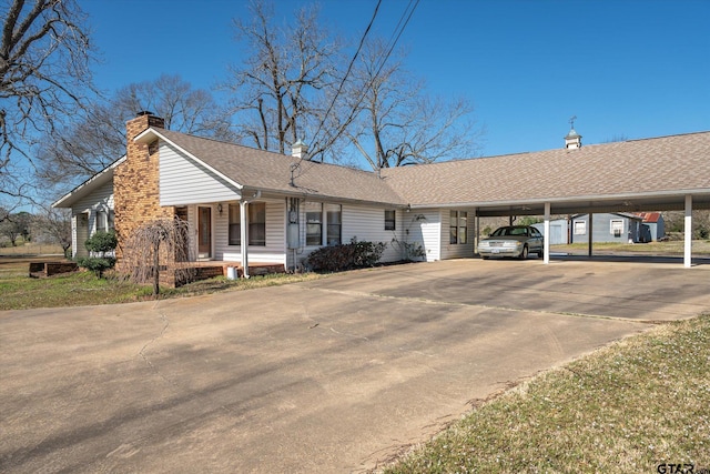 single story home featuring a carport, roof with shingles, concrete driveway, and a chimney