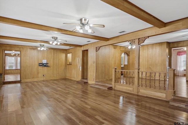 unfurnished living room with wooden walls, wood finished floors, visible vents, stairs, and beamed ceiling