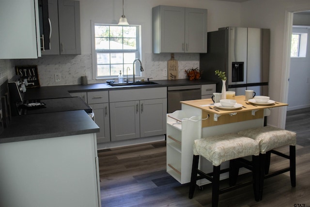 kitchen featuring stainless steel appliances, sink, backsplash, hanging light fixtures, and dark hardwood / wood-style flooring