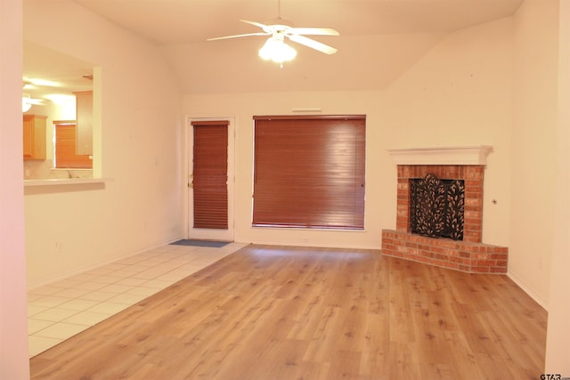 unfurnished living room with vaulted ceiling, a brick fireplace, ceiling fan, and light hardwood / wood-style floors