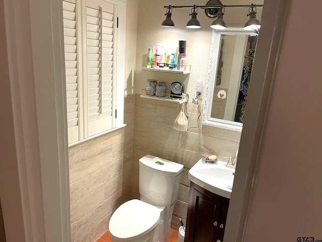 bathroom featuring toilet, vanity, and tile walls